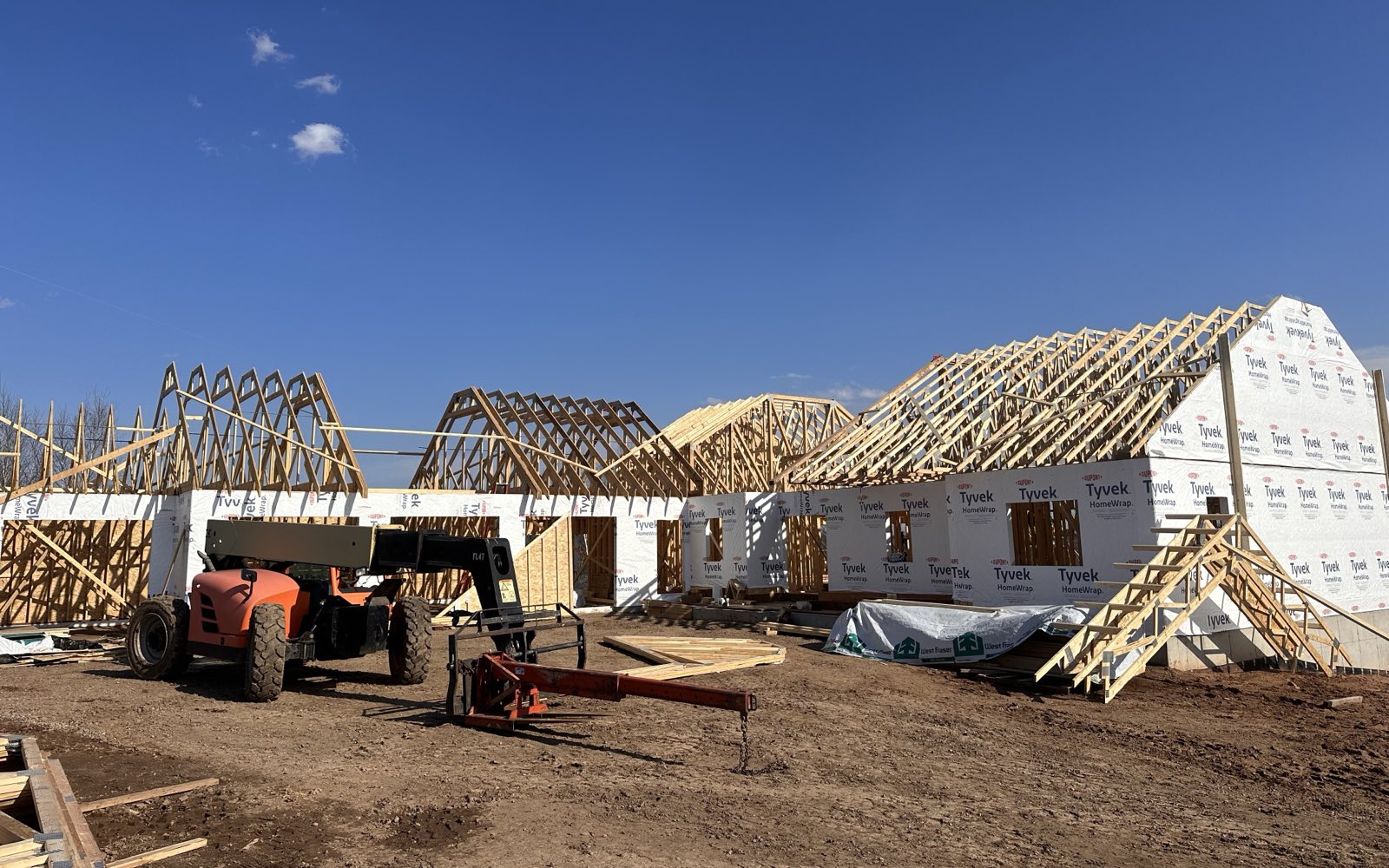 Roof trusses being set on a new single-story home under a clear blue sky