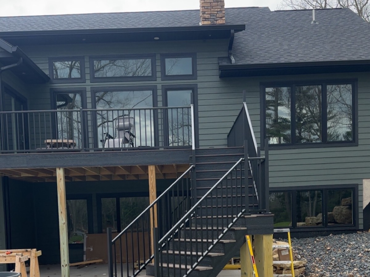 Completed custom home with green lap siding, a covered deck and black railings