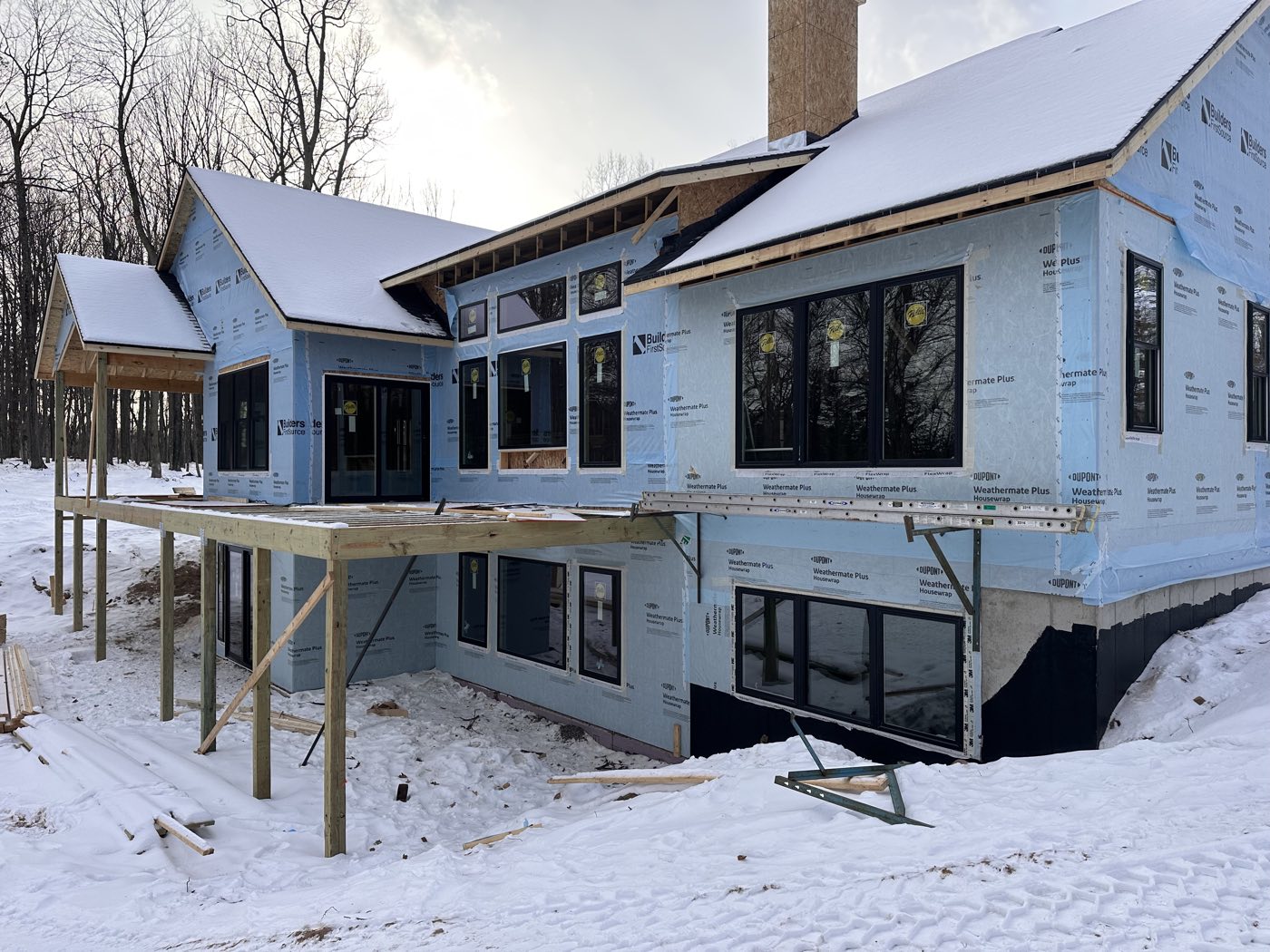 A new home sheathed and weather-wrapped, framing and deck structure visible in winter